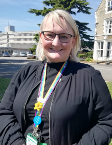Woman with blonde hair and glasses with council offices in the background.