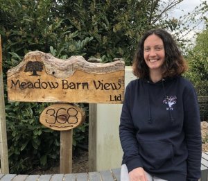 Photo of a woman wearing a navy hoodie posing next to a sign that says 'Meadow Barn View Ltd'